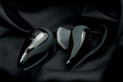 Two sleek black makeup brushes with soft bristles on black fabric.