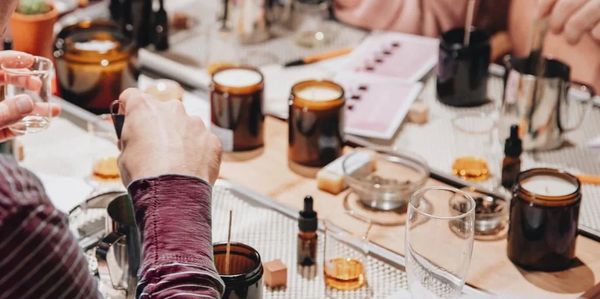 People crafting candles with tools and amber jars on a table.