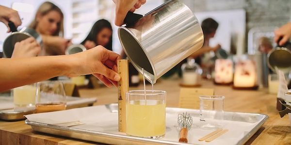 Person pouring liquid into a glass during a candle-making workshop.