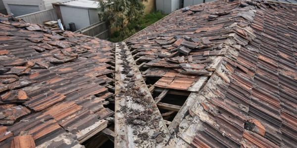 Damaged roof with missing and broken tiles showing structural exposure.