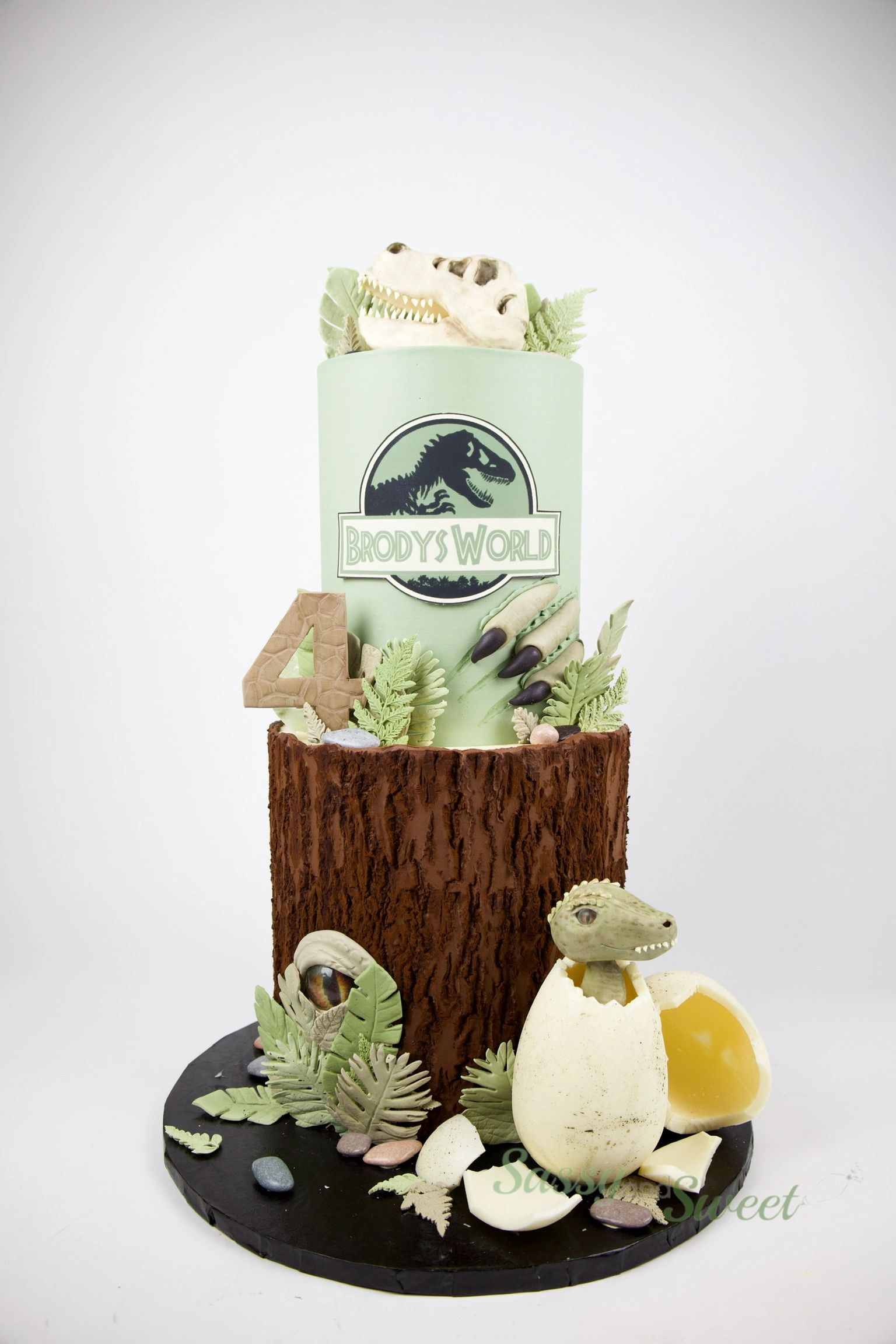 Two-tier Jurassic Park-themed birthday cake with dinosaur details and number 4.