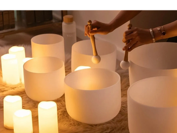Hands playing crystal singing bowls with glowing candles.