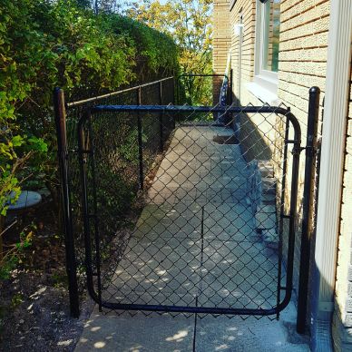 A black chain-link gate on a concrete pathway beside a house.