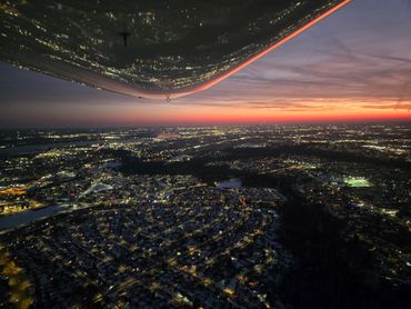 Cityscape at dusk with wing reflection and glowing horizon.