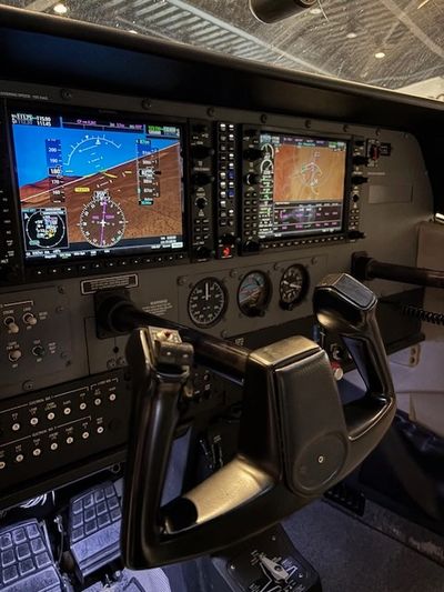 Cockpit view of an aircraft with dual digital displays and control yoke.