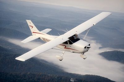 A small white airplane flying over misty mountains.