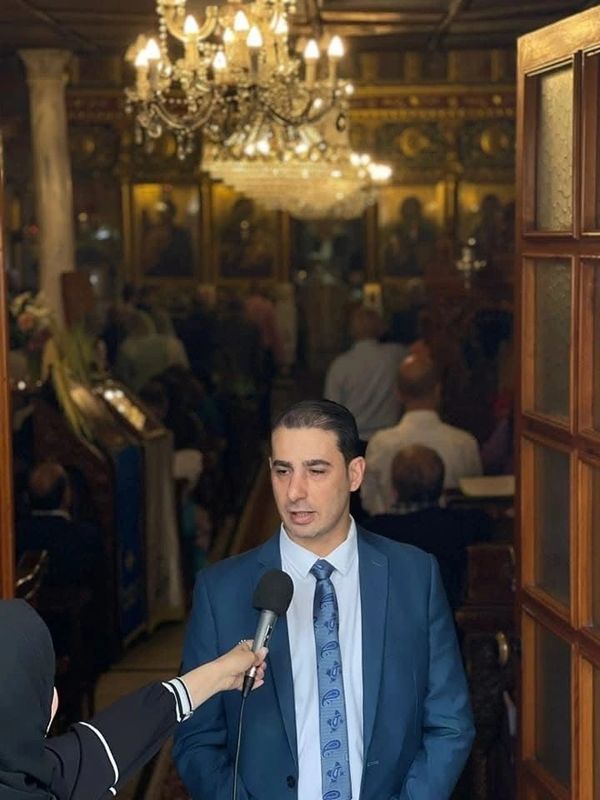 Man in a suit being interviewed inside a church with chandeliers.