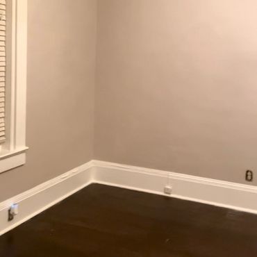 Empty room corner with beige walls and dark wooden floor.