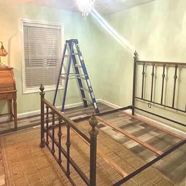 Empty bedroom with an iron bed frame, ladder, and chandelier lighting.