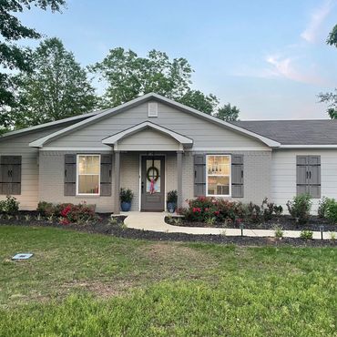 Single-story house with gray shutters, a wreath on the door, and a landscaped front yard with flowers.