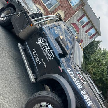 Black tow truck parked on the street with company branding and phone number.