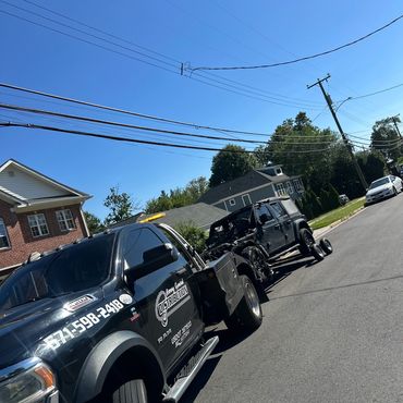 Tow truck hauling a damaged black Jeep on a sunny day.