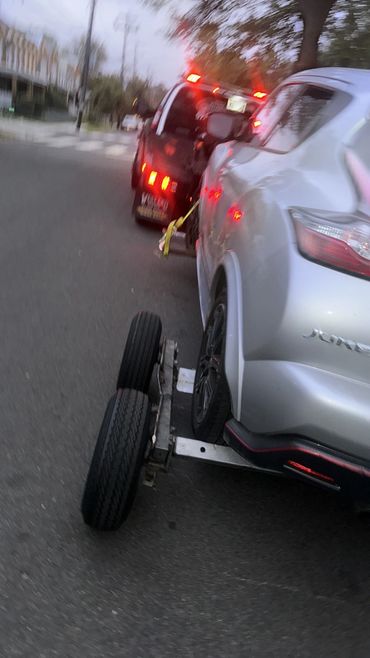 A silver car being towed by a black tow truck on a street.