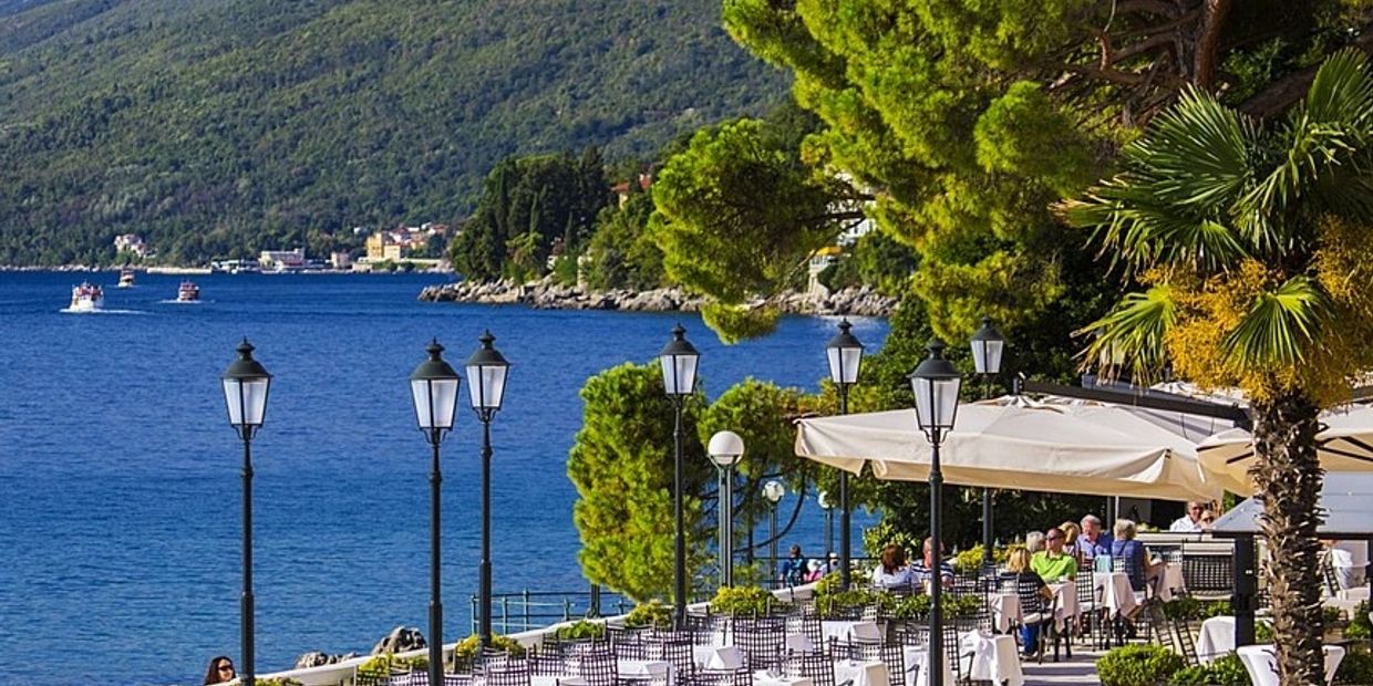 Scenic outdoor dining area by the sea with green hills in the background.