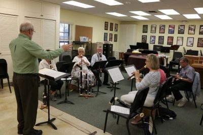 A music instructor directs a small group playing recorders and guitar in a classroom.