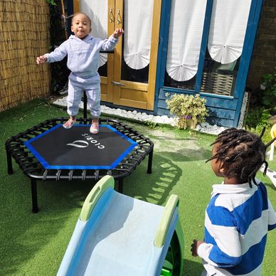 A toddler joyfully jumps on a trampoline while another child watches nearby.