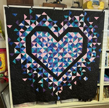 Colorful heart-shaped quilt with geometric patterns on black background.