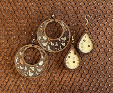 Two pairs of wooden earrings with bird and coffee patterns on a mesh background.
