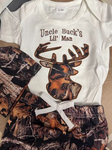 Infant outfit with deer antler design and camouflage pants, labeled 0-3 months.