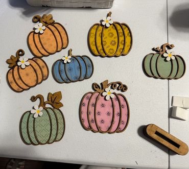 Decorative wooden pumpkins in pastel colors with floral patterns and small white flowers.