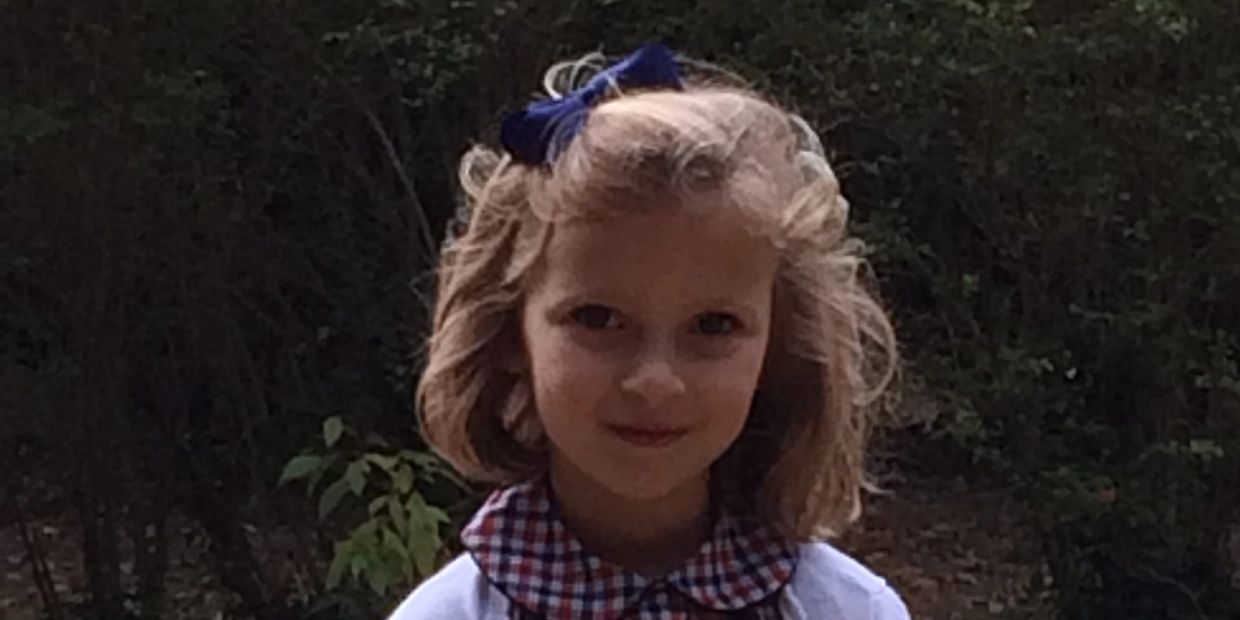 Young girl with curly hair and a blue bow outdoors.
