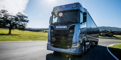 A blue Scania truck driving on a road in daylight.