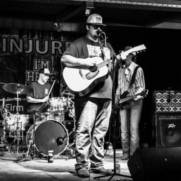 A black-and-white photograph of a band performing on stage at the 2025 Doyle Boil.