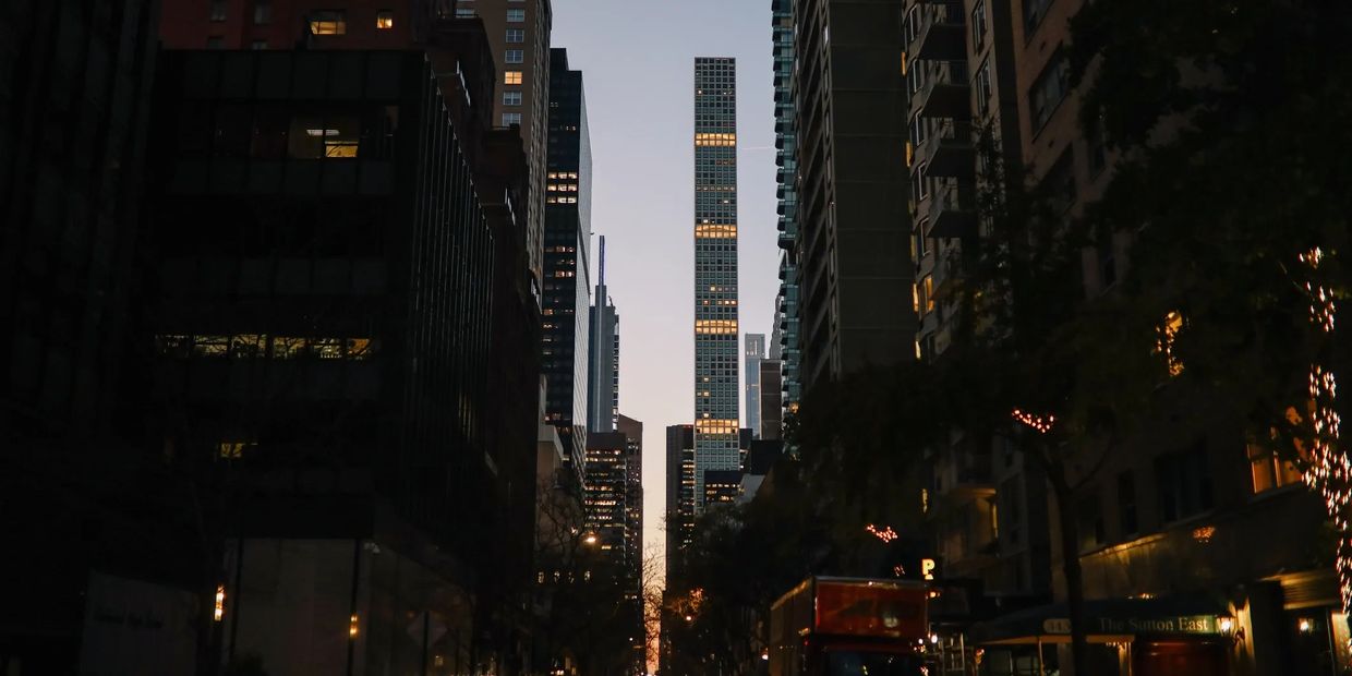 City street at dusk with tall buildings and lights on.