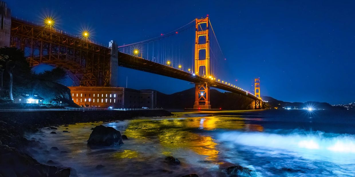 Golden Gate Bridge illuminated at night with reflections on water.