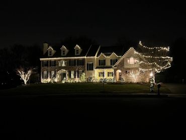 Large house decorated with warm white Christmas lights at night.