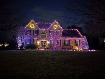 Brick house decorated with colorful Christmas lights at night.