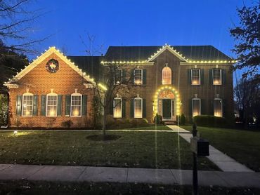 Brick house decorated with Christmas lights and a wreath at twilight.