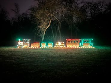 A wooden train decorated with colorful Christmas lights outdoors at night.