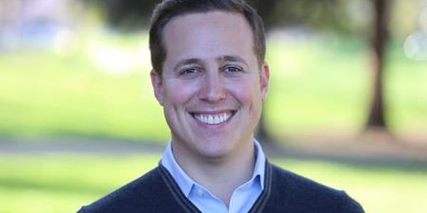 Smiling man outdoors with blurred green background.