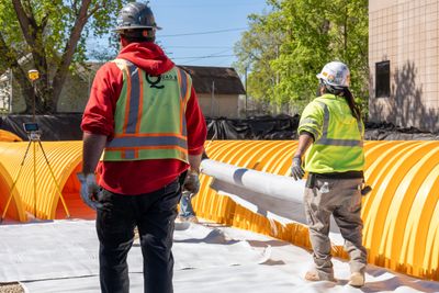 Two construction workers installing a large pipe outdoors.