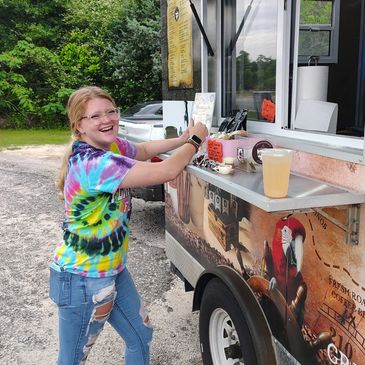 Smiling girl in tie-dye shirt ordering from a food truck outdoors.