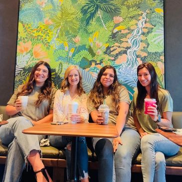 Four women sitting together enjoying colorful drinks at a cafe.