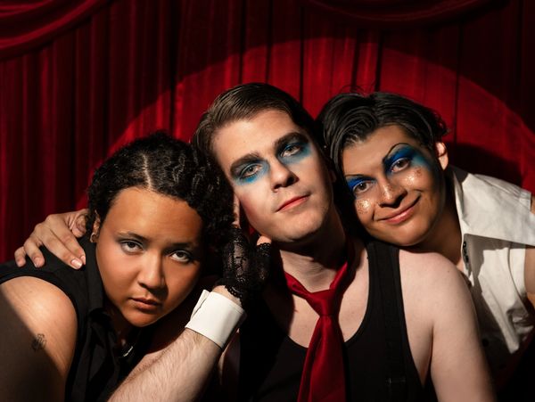 Three people with dramatic blue eye makeup posing against a red curtain.