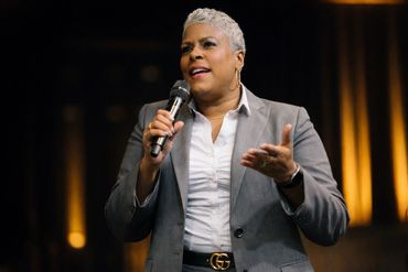 A woman in a gray suit speaking into a microphone on stage.