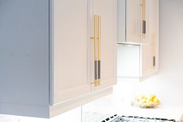 White kitchen cabinets with modern gold handles and a fruit bowl on the counter.