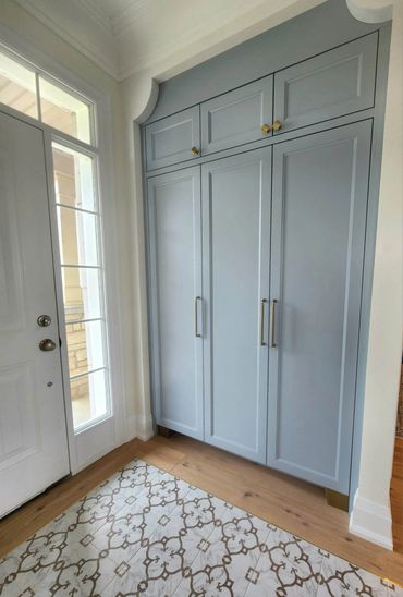 Elegant blue built-in cabinet with brass handles near a white door and patterned floor tiles.