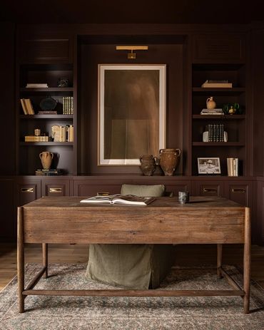 Cozy home office with wooden desk and dark built-in bookshelves.