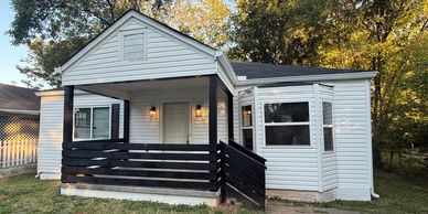 Small white house with black porch railing in a green yard.