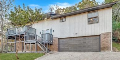 Two-story house with elevated wooden deck and large driveway.