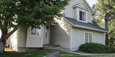 A two-story house with beige siding surrounded by trees and lawn.