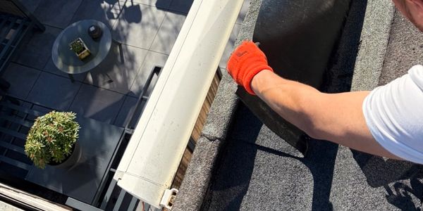 Person installing or repairing a roof gutter wearing an orange glove.