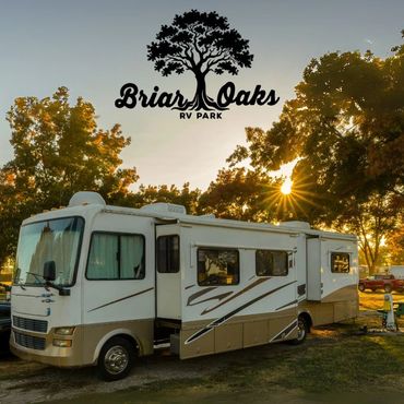 RV parked at Briar Oaks RV Park during sunset among trees.