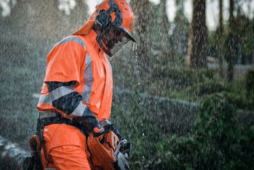 Worker in orange rain gear holding a chainsaw in heavy rain.