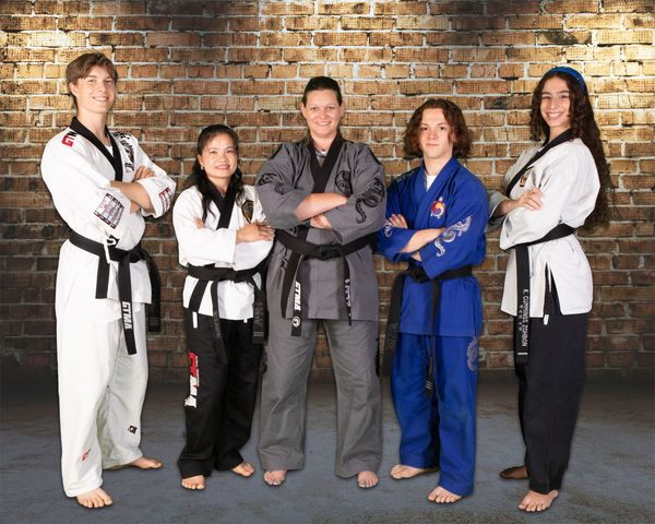 Group of five martial artists in uniforms posing with arms crossed.