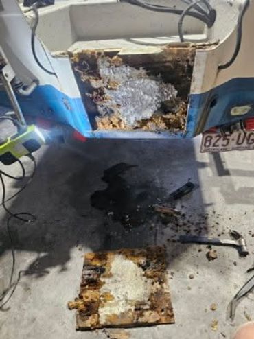 Damaged boat hull with removed rotten wood and tools nearby.